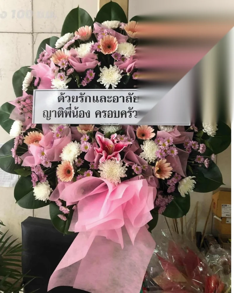 พวงหรีดดอกไม้สดจัดใหม่พร้อมป้ายชื่อผู้ส่งตั้งอยู่หน้าศาลาวัด