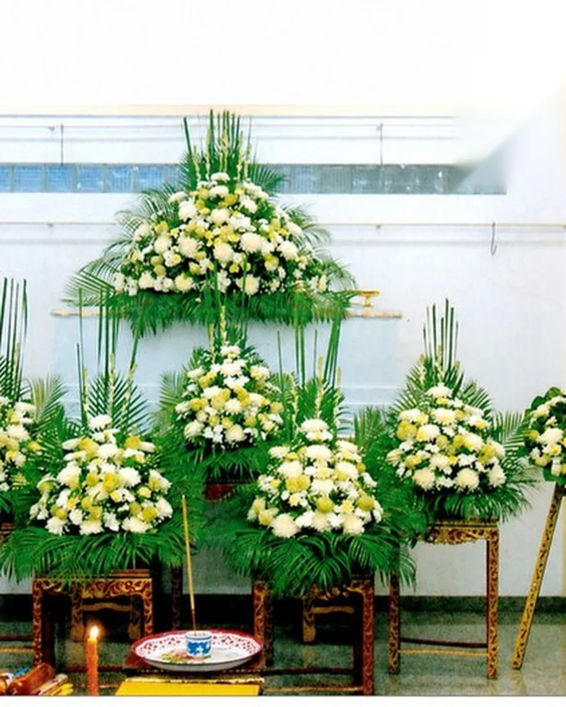 ดอกไม้ไว้อาลัยโทนขาวเขียวจัดเป็นสามชุดวางเรียงในห้องพิธี