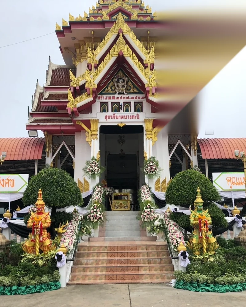 ศาลาการเปรียญของวัดไทยประดับดอกไม้ไว้อาลัยด้านหน้าทางขึ้น